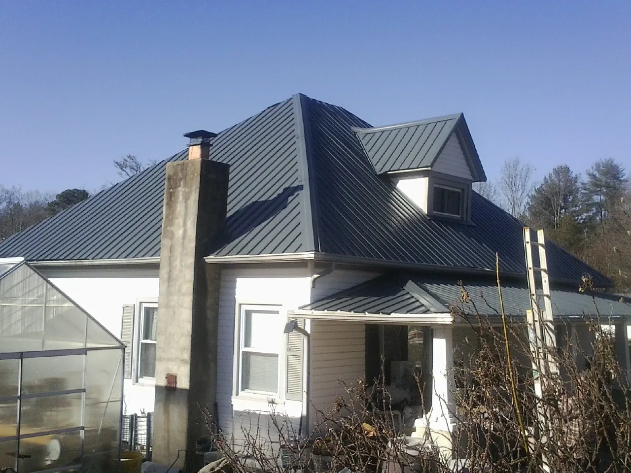 Dark blue standing seam metal roof on a white farmhouse with dormer — Slate & Tile Roof Repair by Roofing Brothers in Summerdale