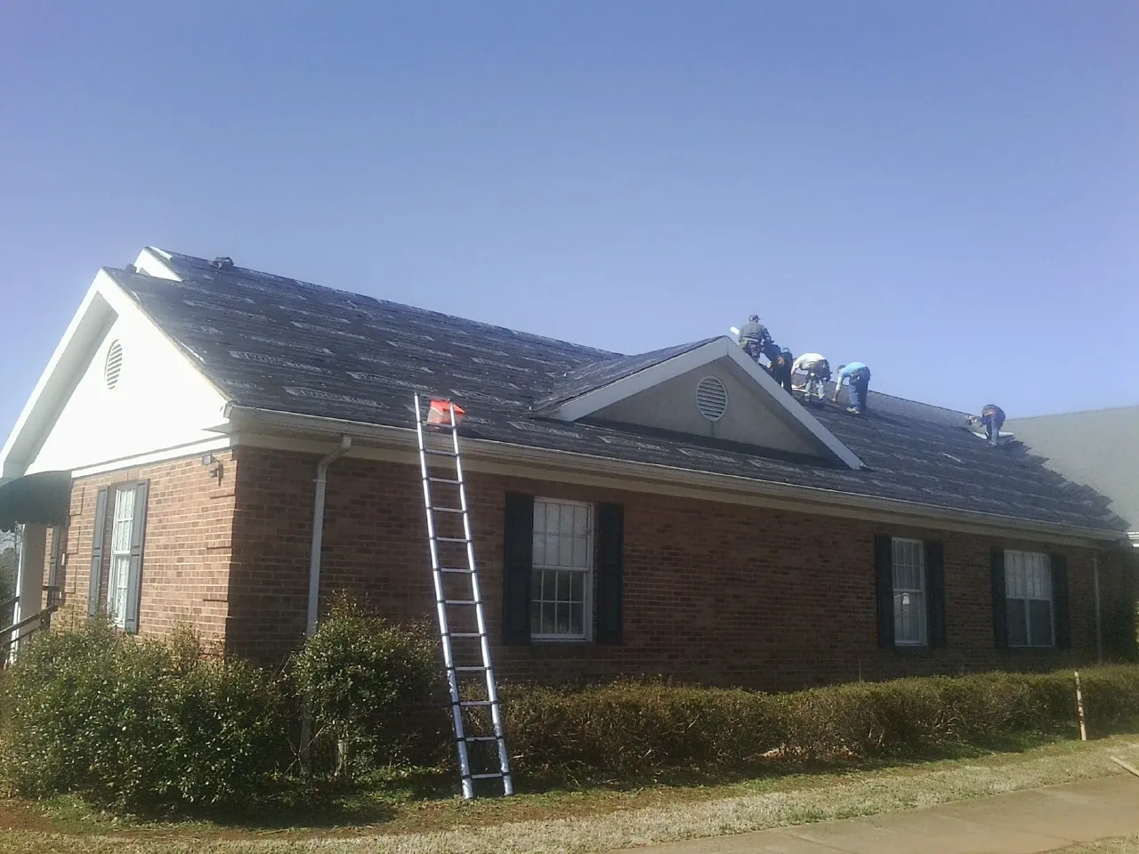 Crew tearing shingles off a brick ranch roof with a ladder set — Metal Roof Repair work by our crew in Summerdale