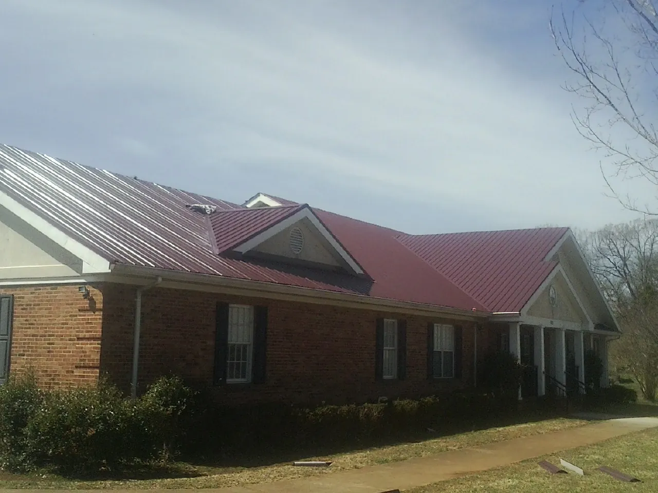 Red metal roof with gabled entries on a long brick building, from a Hail Damage Roof Repair job in Summerdale