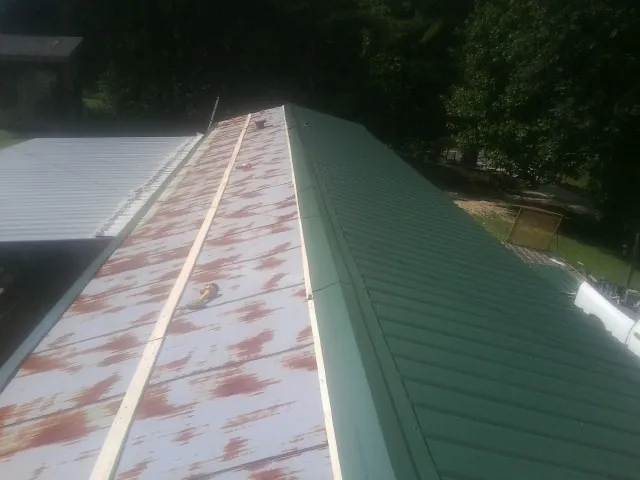 Old rusted panels beside newly installed green metal roofing — Wind Damage Roof Repair by Roofing Brothers in Summerdale
