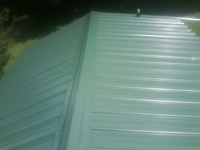 New green metal panels meeting at the ridge of a roof — Flat Roof Repair work by our crew in Summerdale