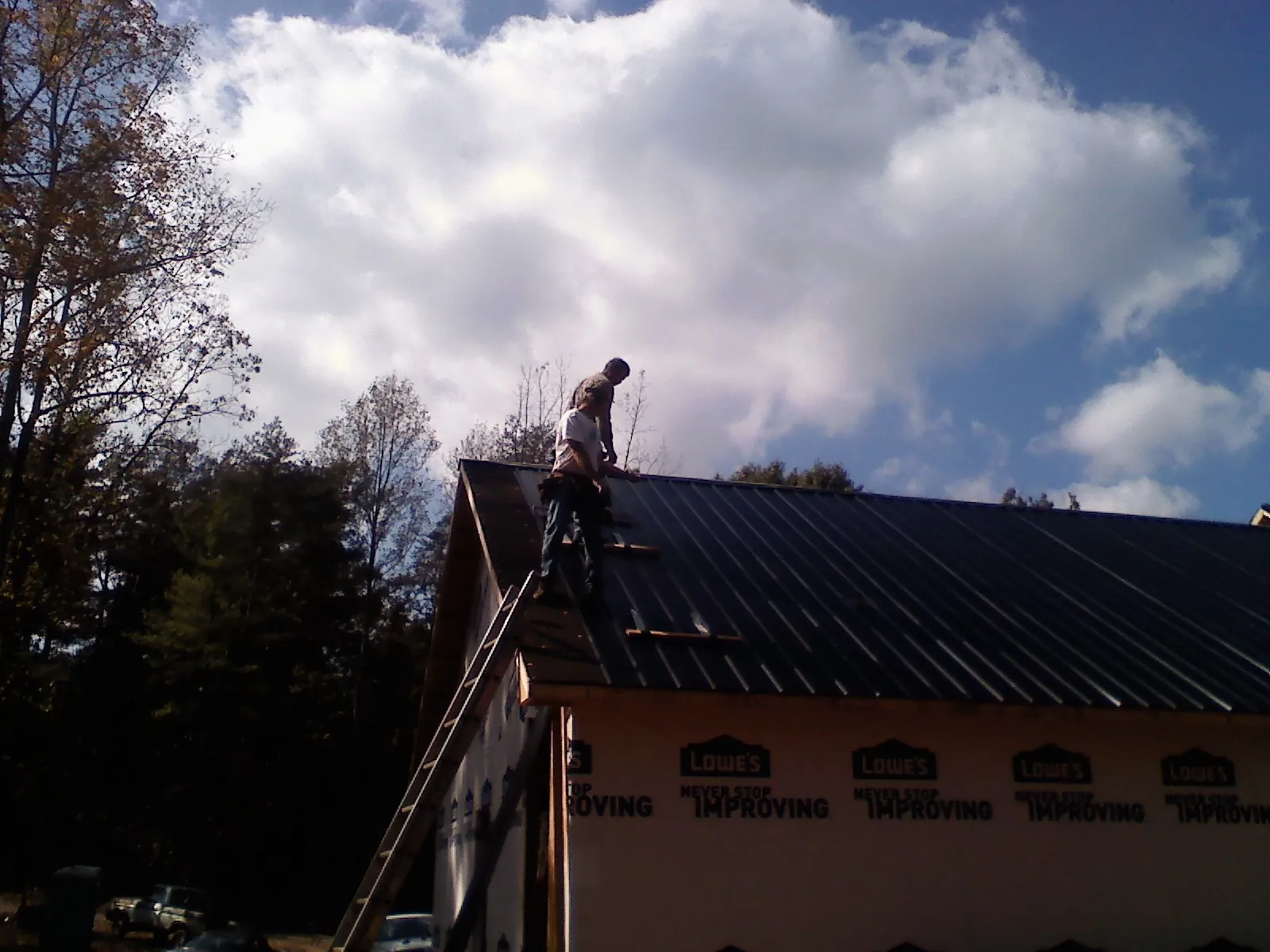 Roofer fastening dark metal panels high against a cloudy sky, from a Roof Inspection job in Summerdale