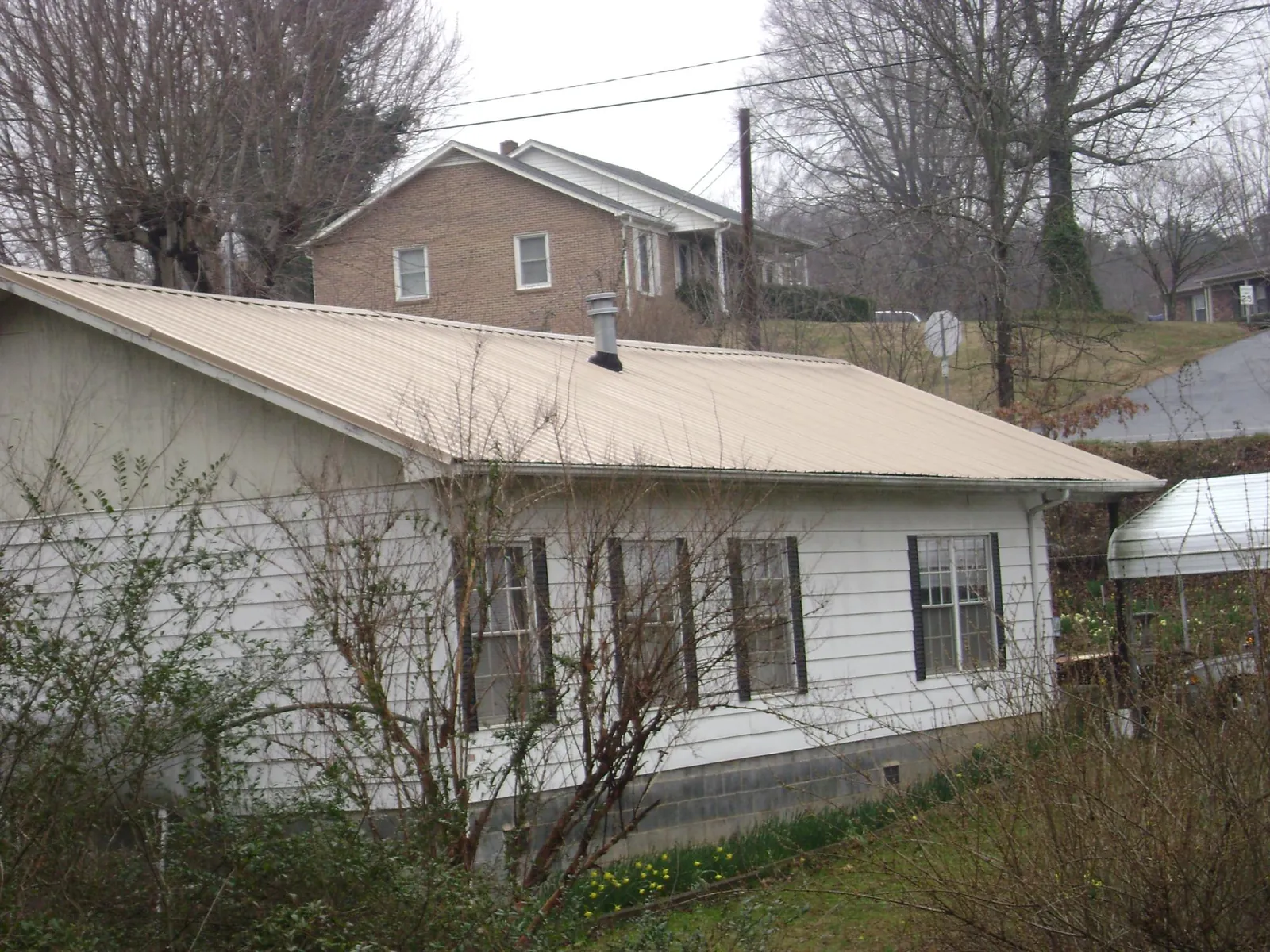 Tan metal roof on a white sided house set into a hillside — Commercial Roofing by Roofing Brothers in Summerdale